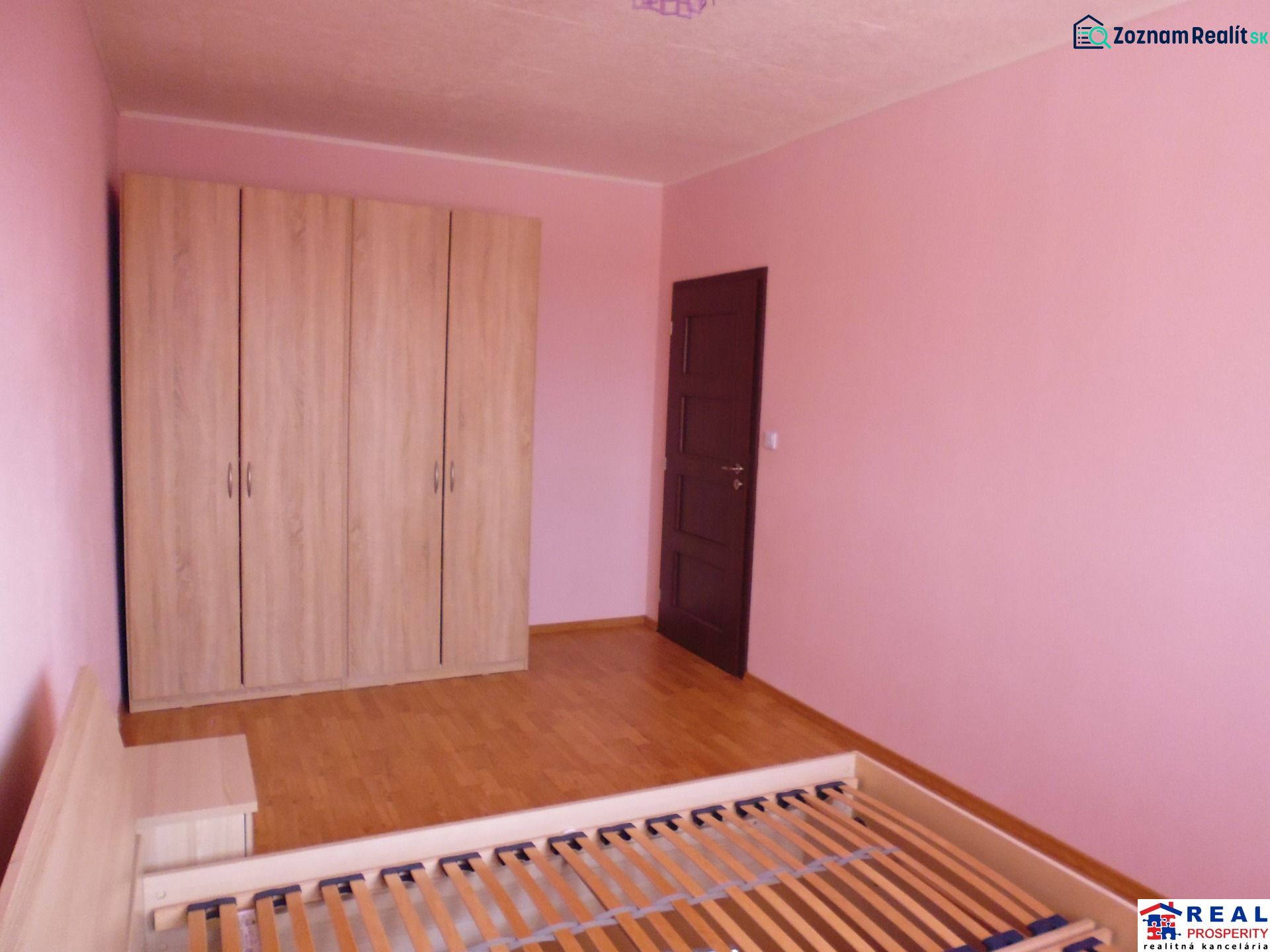 A room in a 2-room apartment with pink walls, a wardrobe, and a floor with a wooden decor.