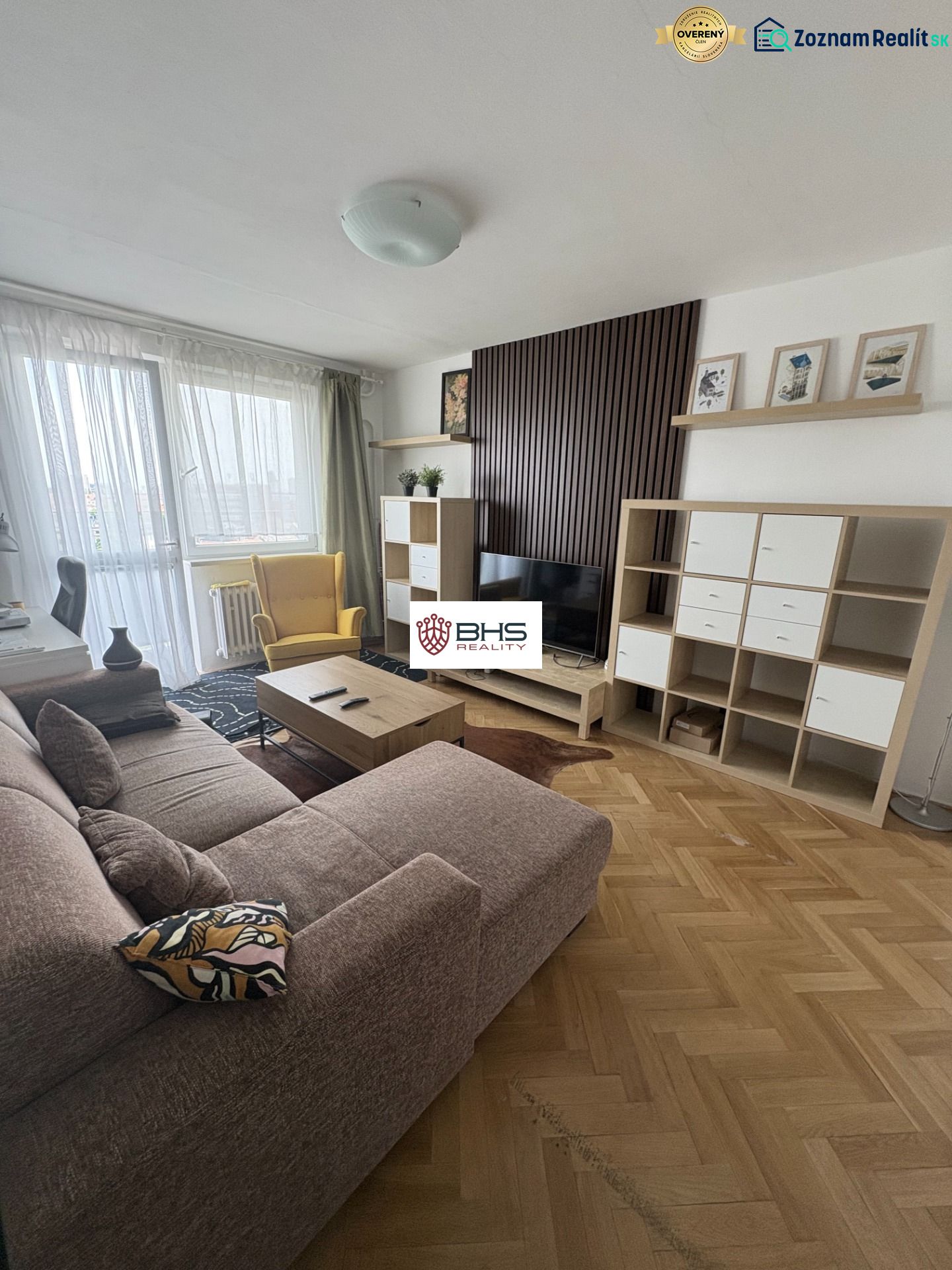 Living room in a two-room apartment with a wood-patterned floor, sofa, and TV cabinet.