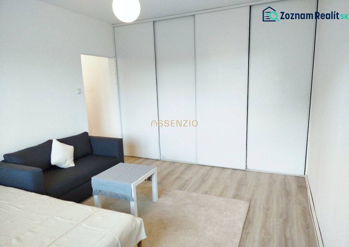 A room in a one-bedroom apartment with a sofa, a table, and a wooden decor floor.