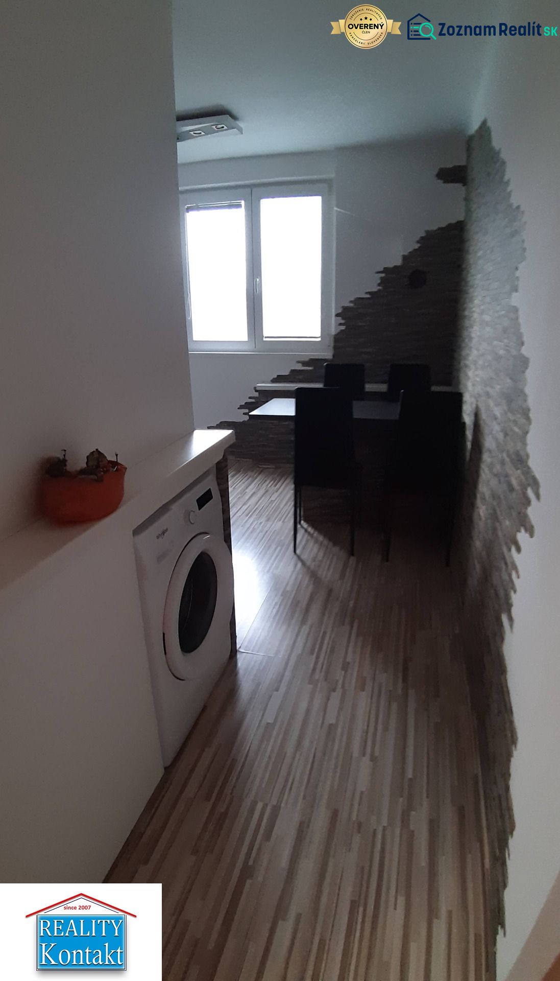 Dining area with wood-patterned flooring, a washing machine, and an interesting wall in a 2-room apartment.