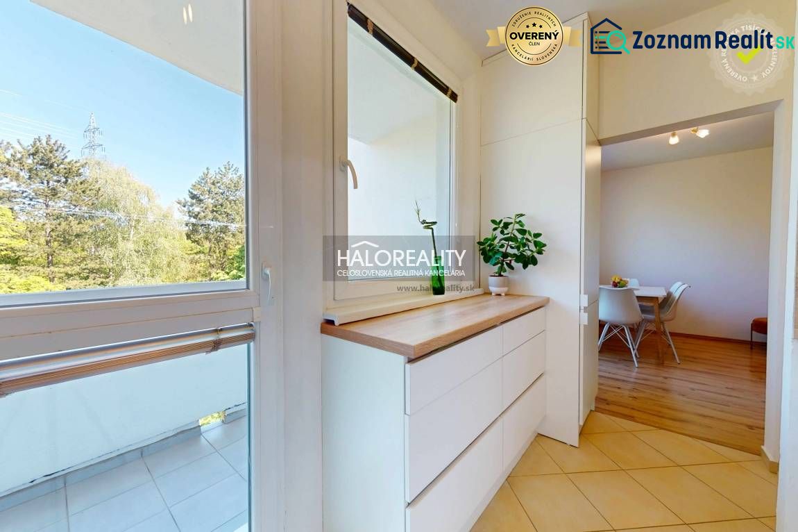 A kitchen in a 3-room apartment with white furniture and a view of the surroundings.