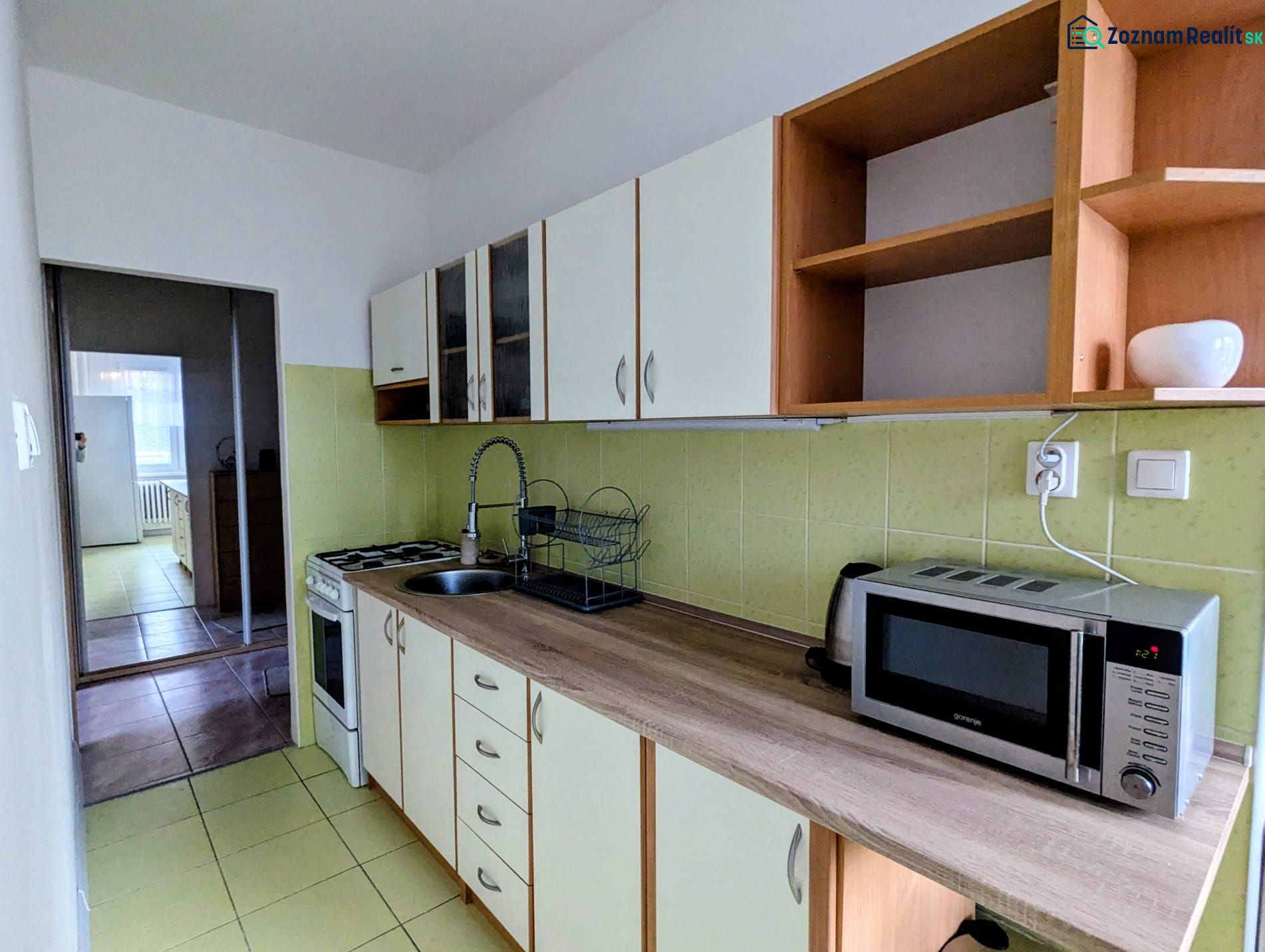 A kitchen in a 2-room apartment with a microwave and a stovetop, leading into another room.