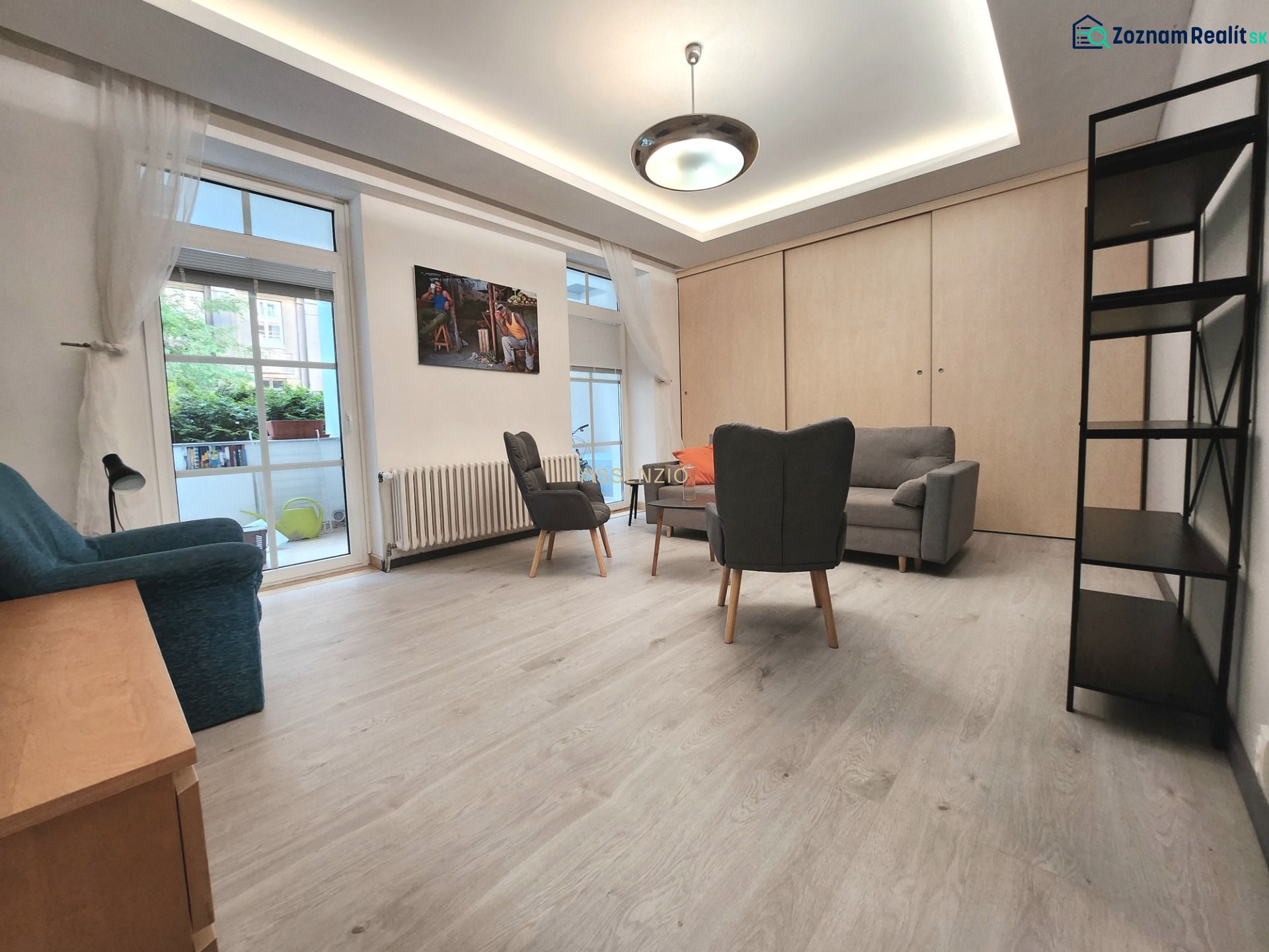 Living room in a two-room apartment, wooden decor flooring, furniture, large windows.