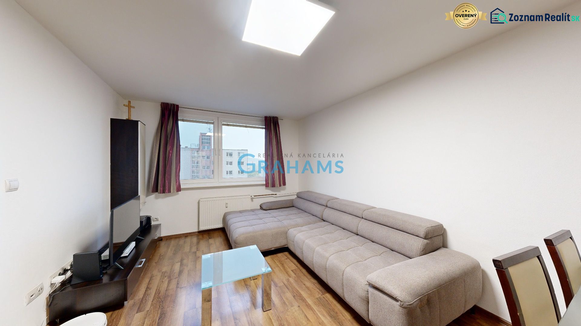 Living room with a gray sofa and wood-patterned flooring in a three-room apartment.