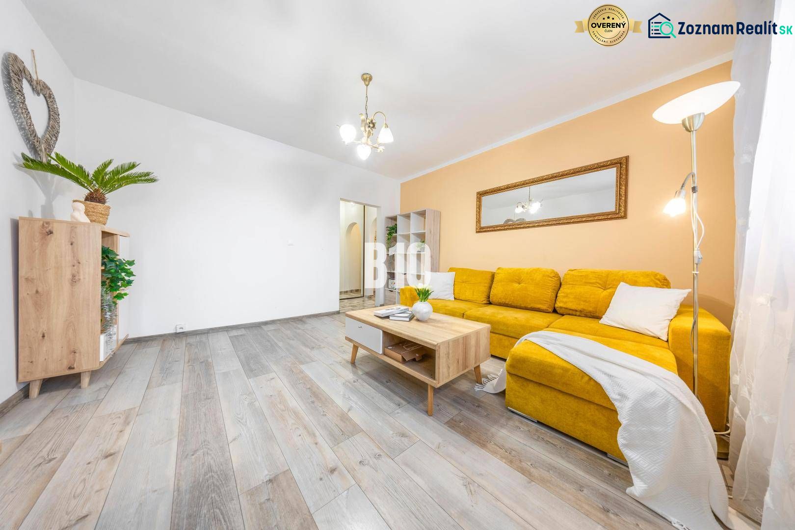 A living room in a two-room apartment with a wooden decor floor and a yellow sofa.