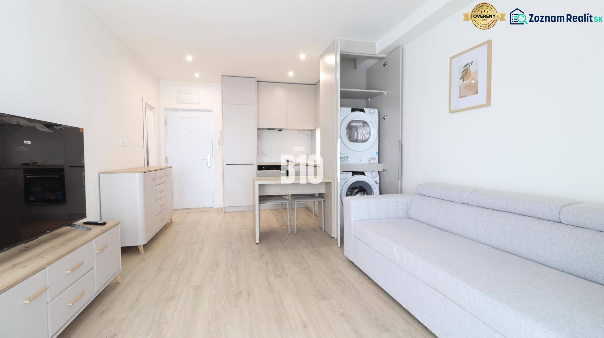 Interior of a 1-room apartment with a kitchen unit, sofa, and washing machine on a floor with a wooden decor.