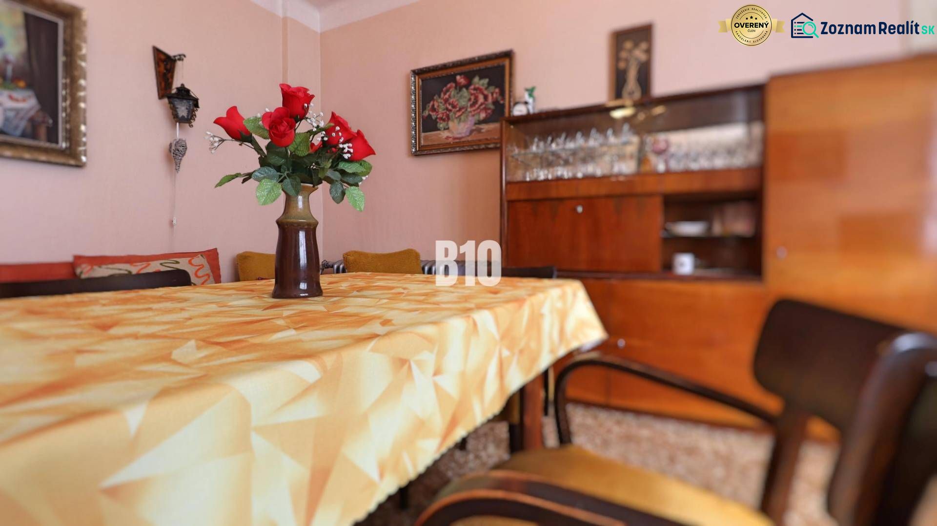 A dining room in a family house with flowers on the table, retro furniture, and glasses in the cabinet.