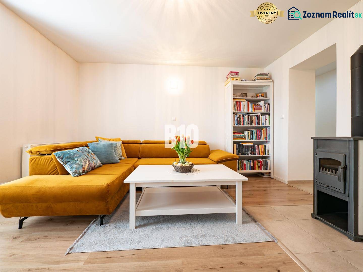 Living room in a 3-room apartment with a mustard sofa, a bookshelf, and a tiled stove.