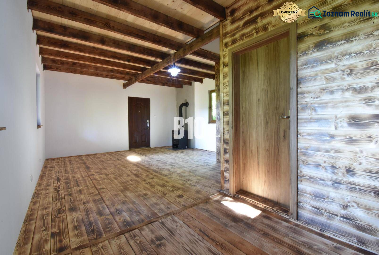 Interior of a cabin with wooden beams, flooring, and a stove for heating.