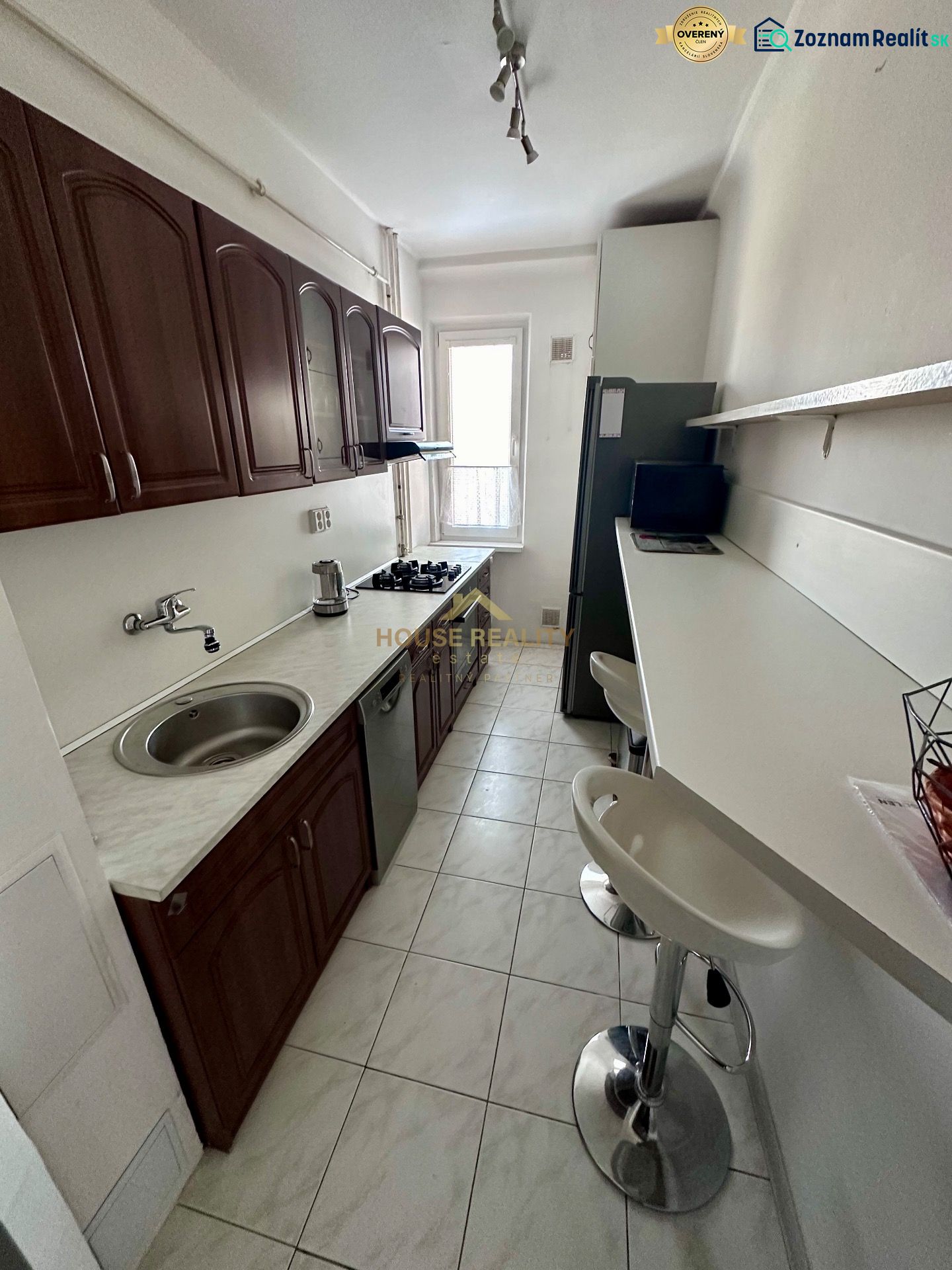A narrow kitchen with a white countertop and wooden cabinets in a 3-room apartment.