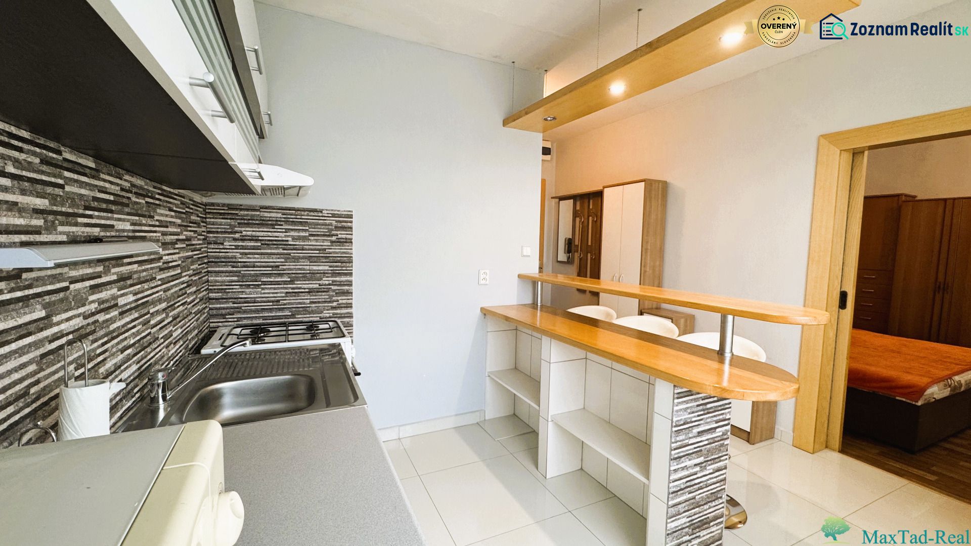 A kitchen in a studio apartment with a bar counter and a wooden decor floor.