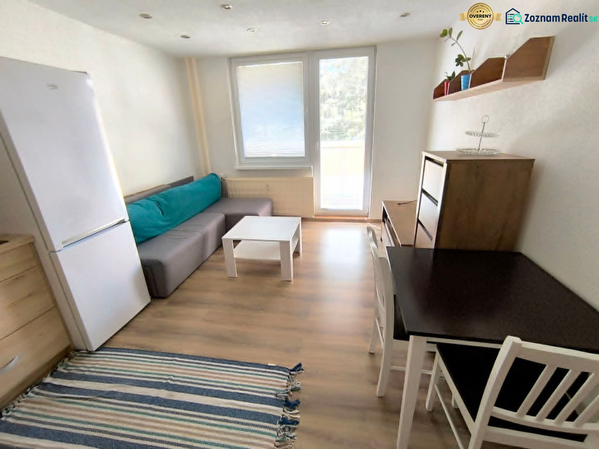 Living area in a studio apartment with wood-patterned flooring, a couch, and a table.