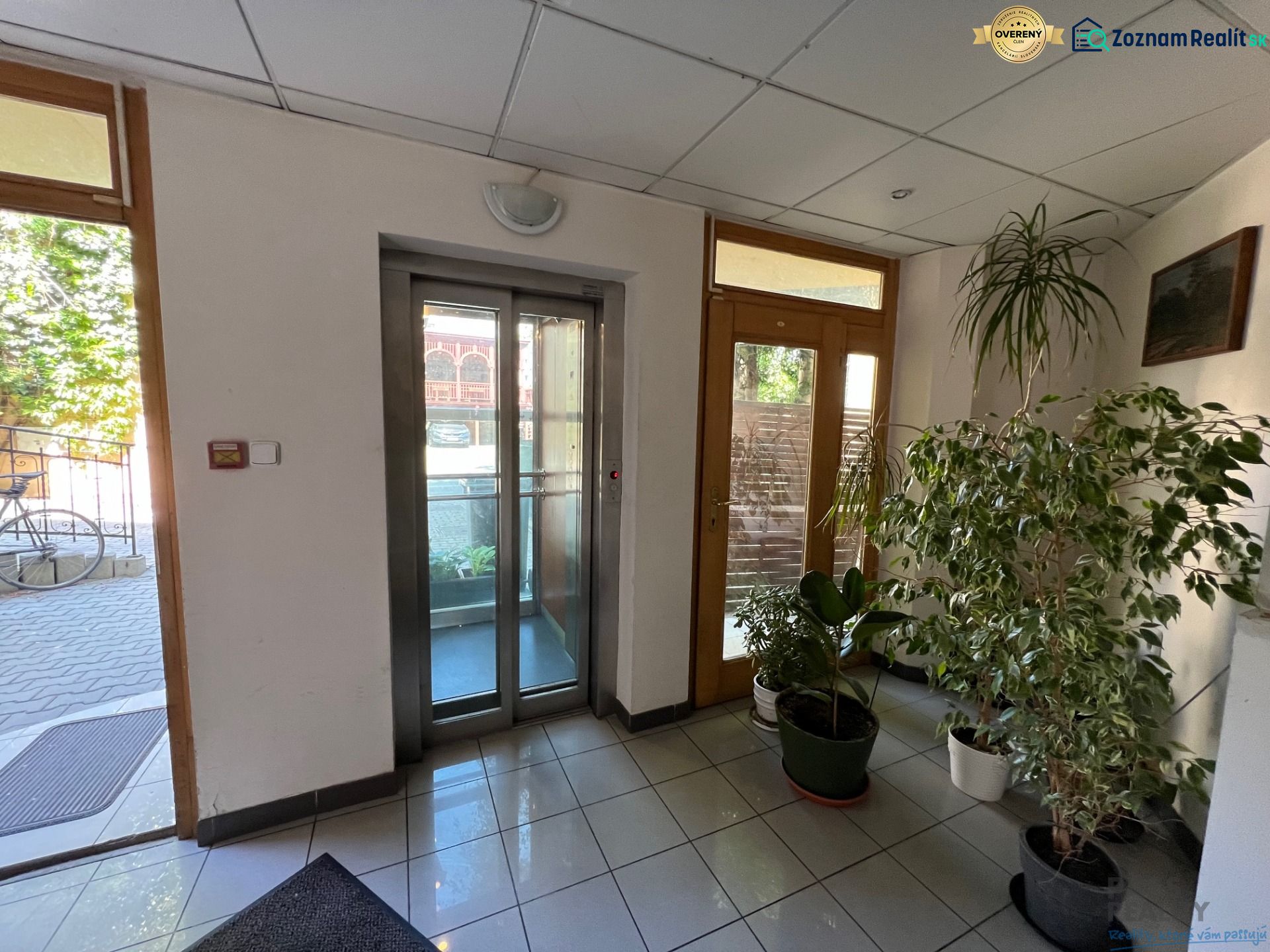 Office interior with tiled floor, elevator, and potted plants.