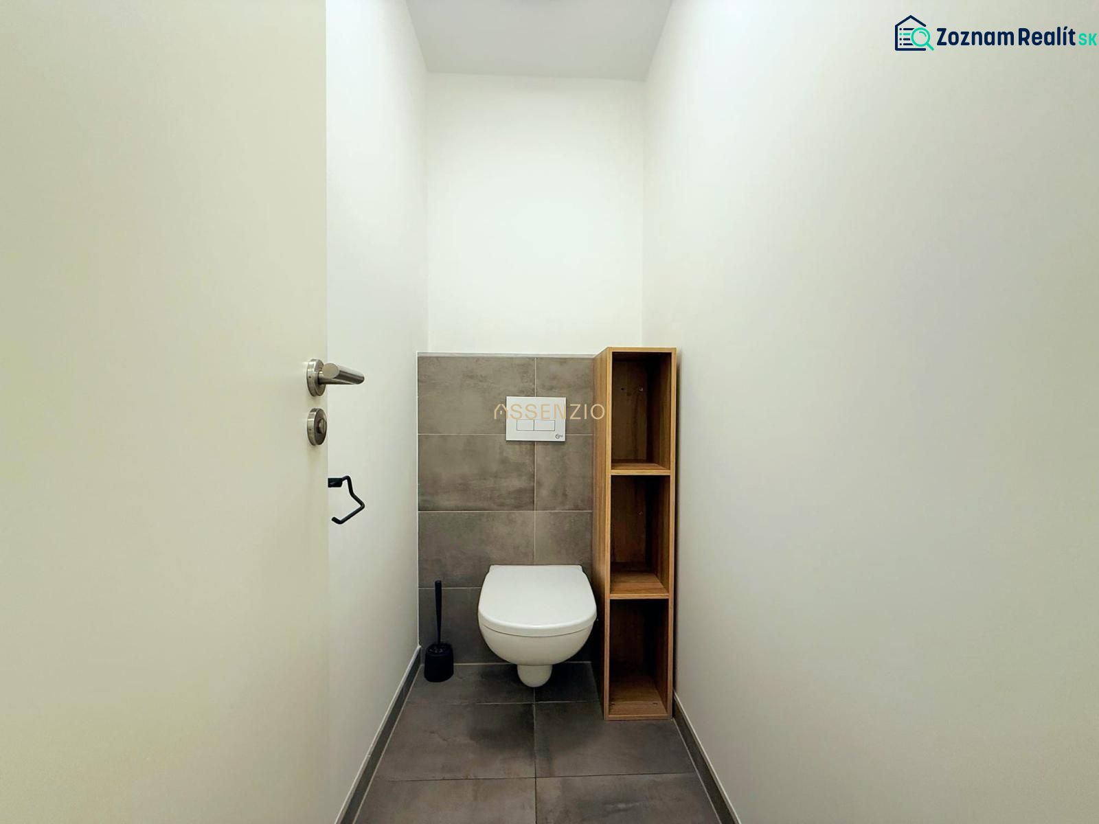 A toilet with gray tiles and a wooden shelf in a two-room apartment.