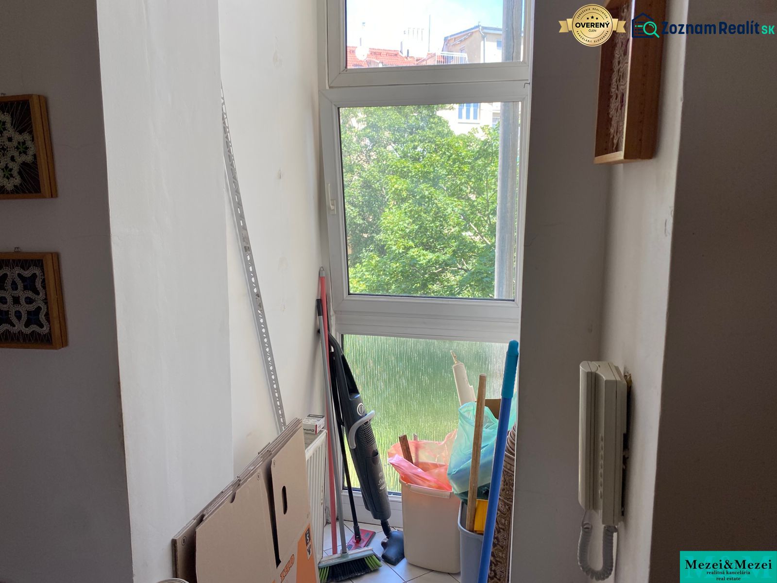 The window section of a 2-room apartment with cardboard boxes, cleaning supplies, and an intercom.