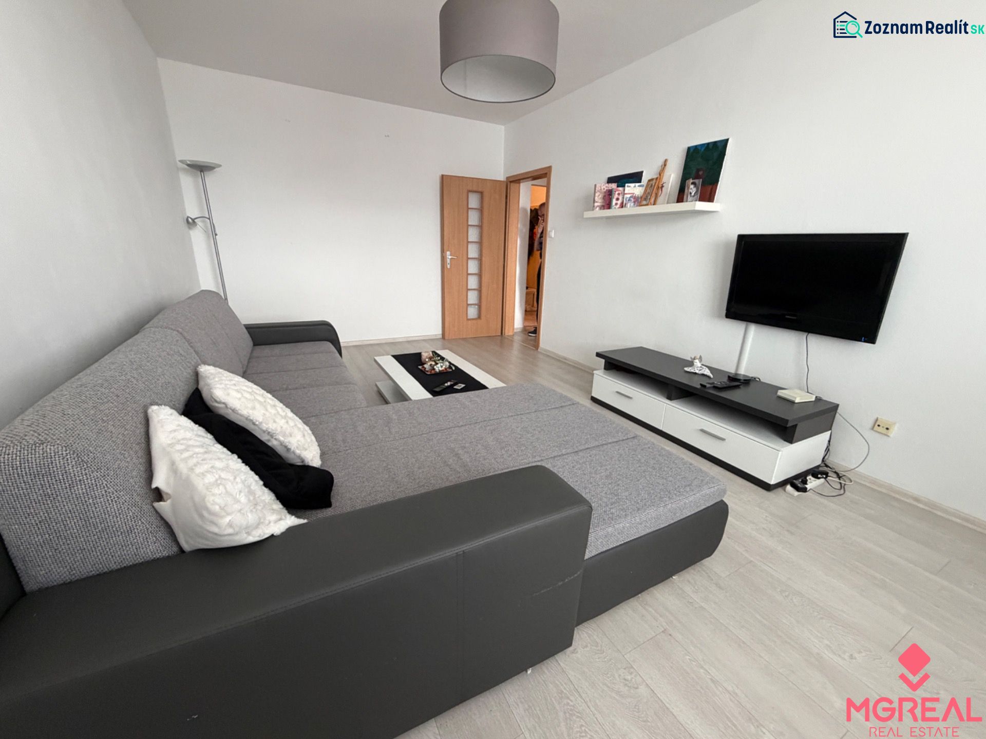 Living room in a two-room apartment with a wooden decor floor and a corner sofa.