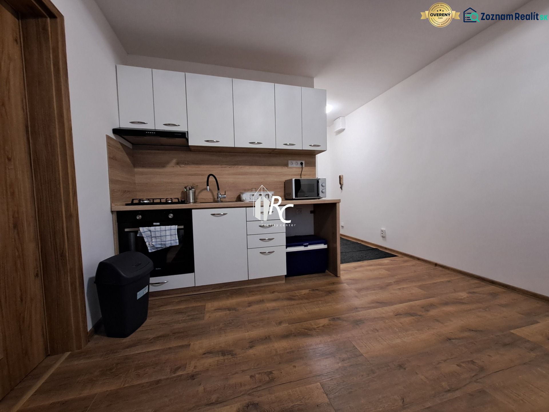Kitchen unit in a studio apartment with wood-patterned flooring and appliances.