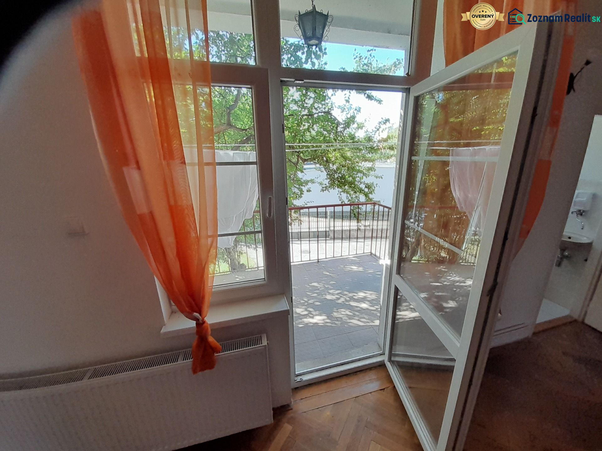 Open balcony with a view and orange curtains, floor with wooden decor.