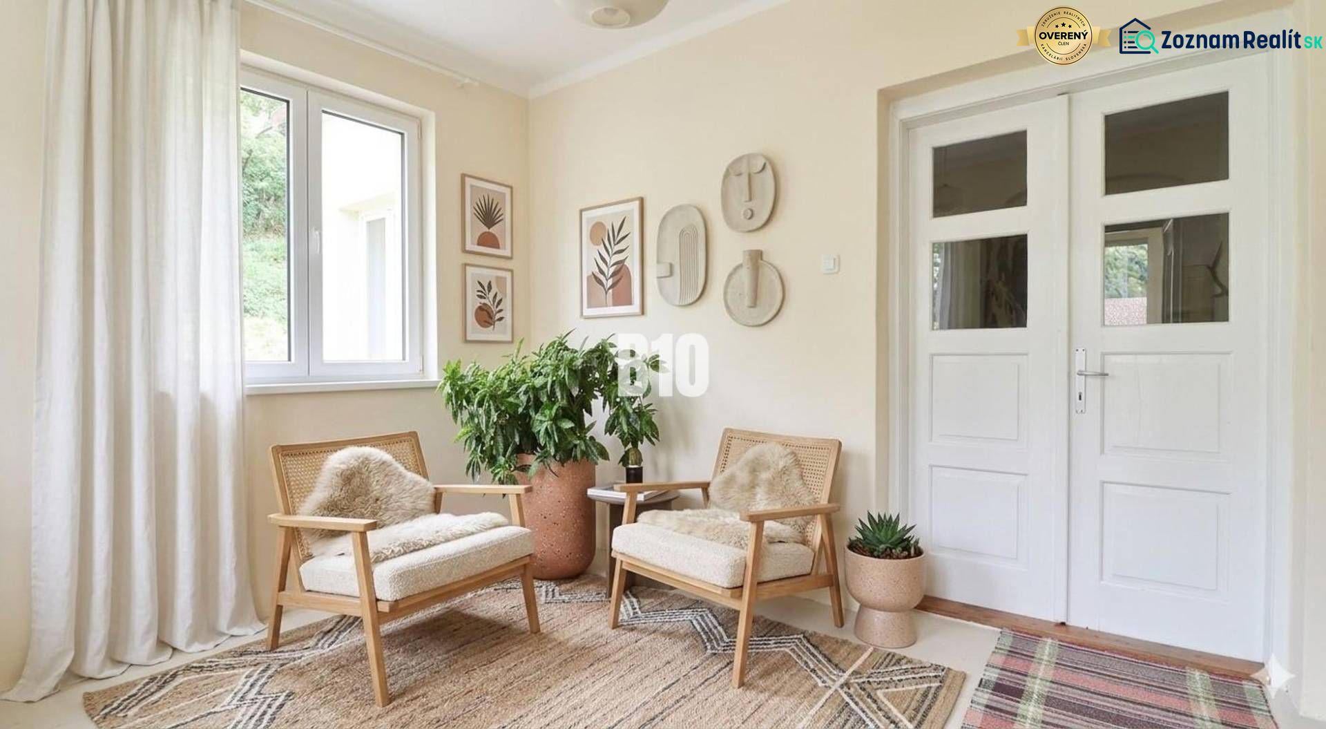 Interior of a family house with light-colored armchairs, greenery, and decorative paintings on the walls.