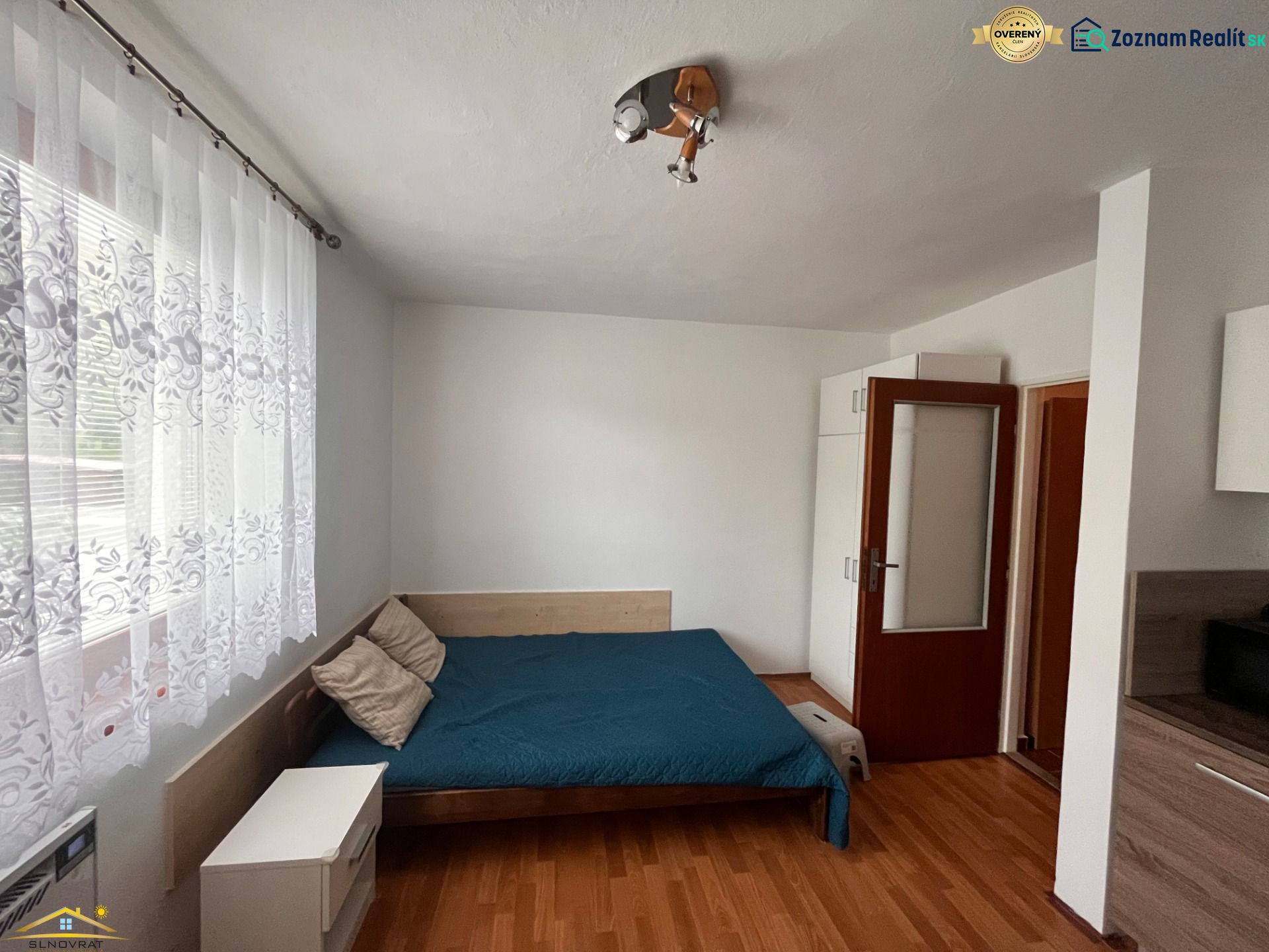 Studio apartment with curtains, bed, and wooden decor flooring.