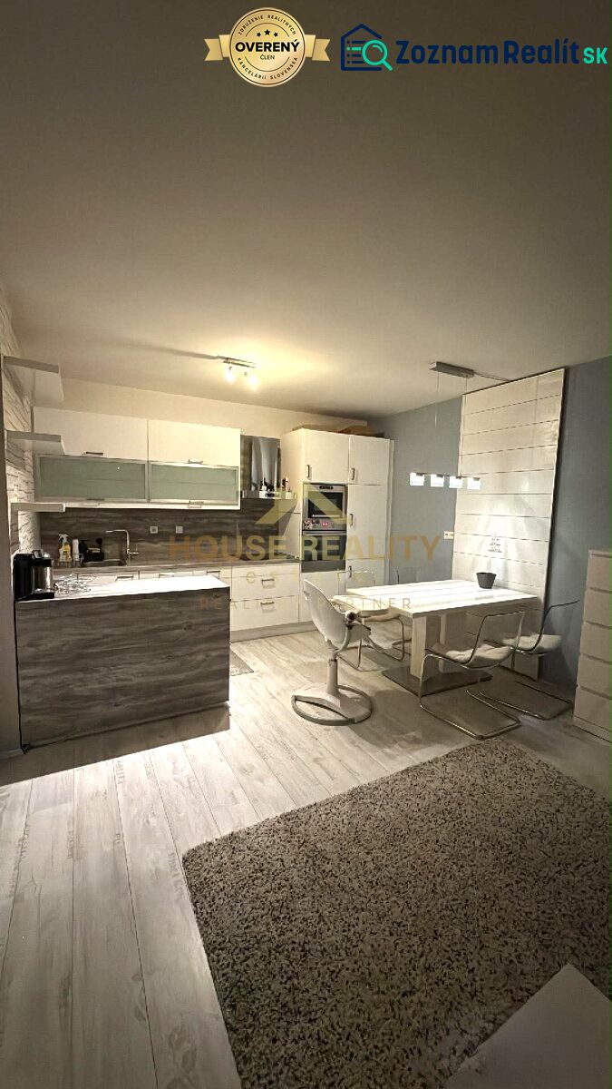 A kitchen area in a two-room apartment with a wood-patterned floor, a dining table, and a kitchen unit.