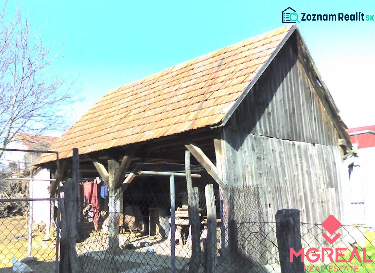 A wooden shed next to a family house in Nové Sady with a red tile roof.
