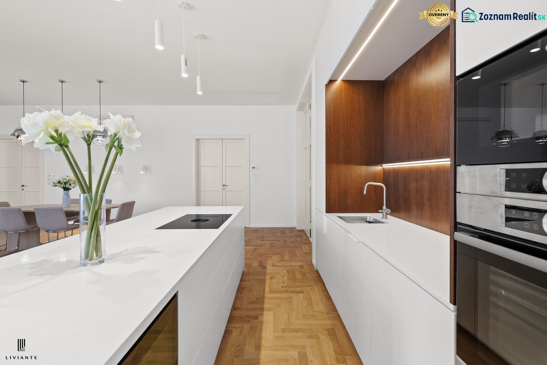 A kitchen in a 4-room apartment with a wooden decor floor, white cabinets, and a dining table.