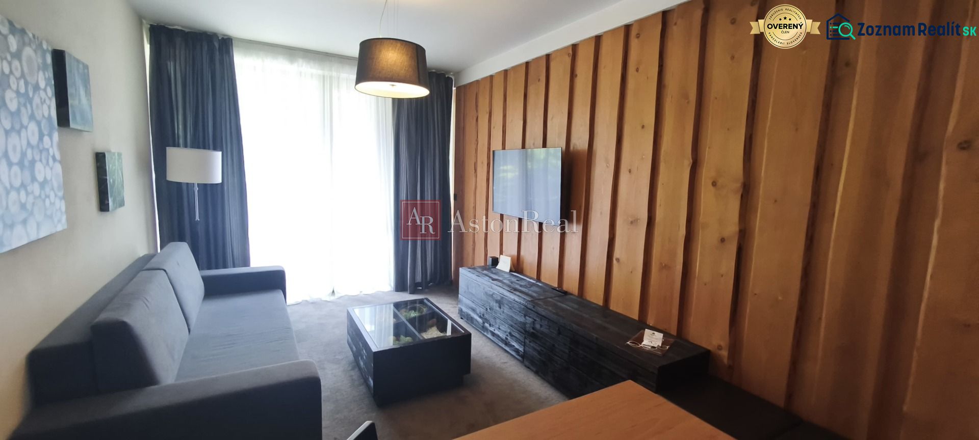 Living room in a holiday apartment with a sofa, wooden wall, and television.