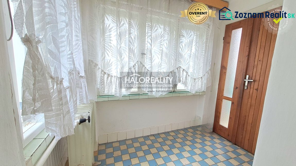 A small hallway in a family house with a tiled floor and curtains on the window.