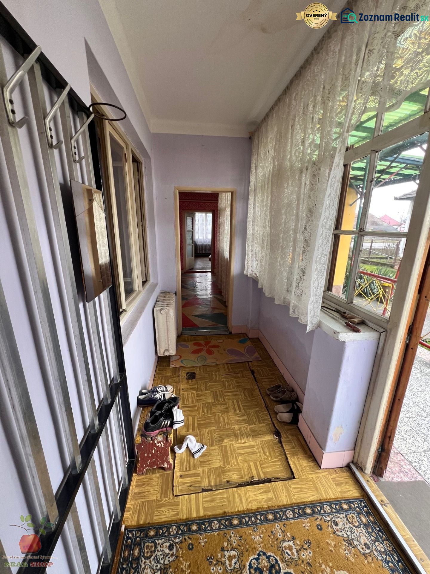 Chodba rodinného domu s topánkami, podlaha s dreveným dekorom, záclony a koberček.