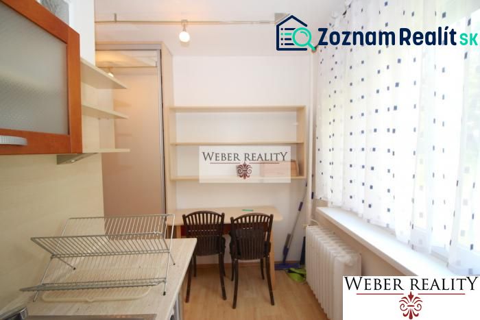 A kitchen in a one-room apartment with shelves, a table, and two chairs.