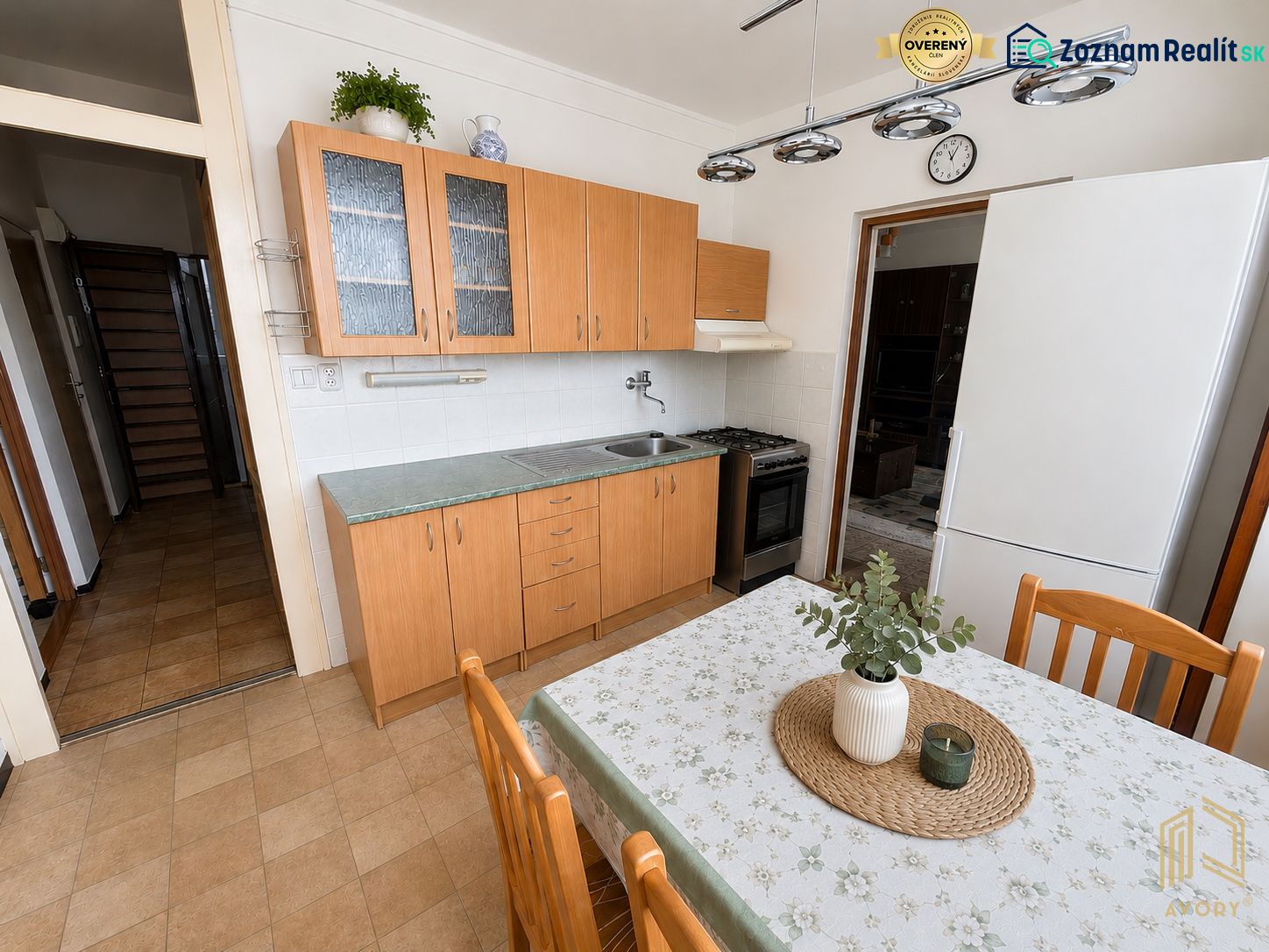 A kitchen in a 3-room apartment with ceramic flooring, wooden furniture, and white walls.