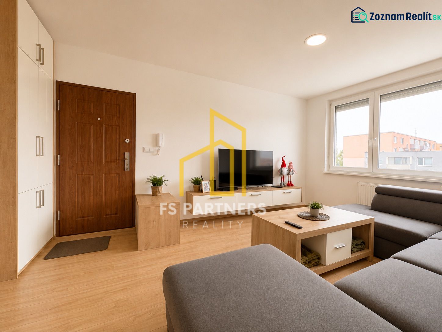 Living room of a three-room apartment with a wooden decor floor, gray sofa, and television.