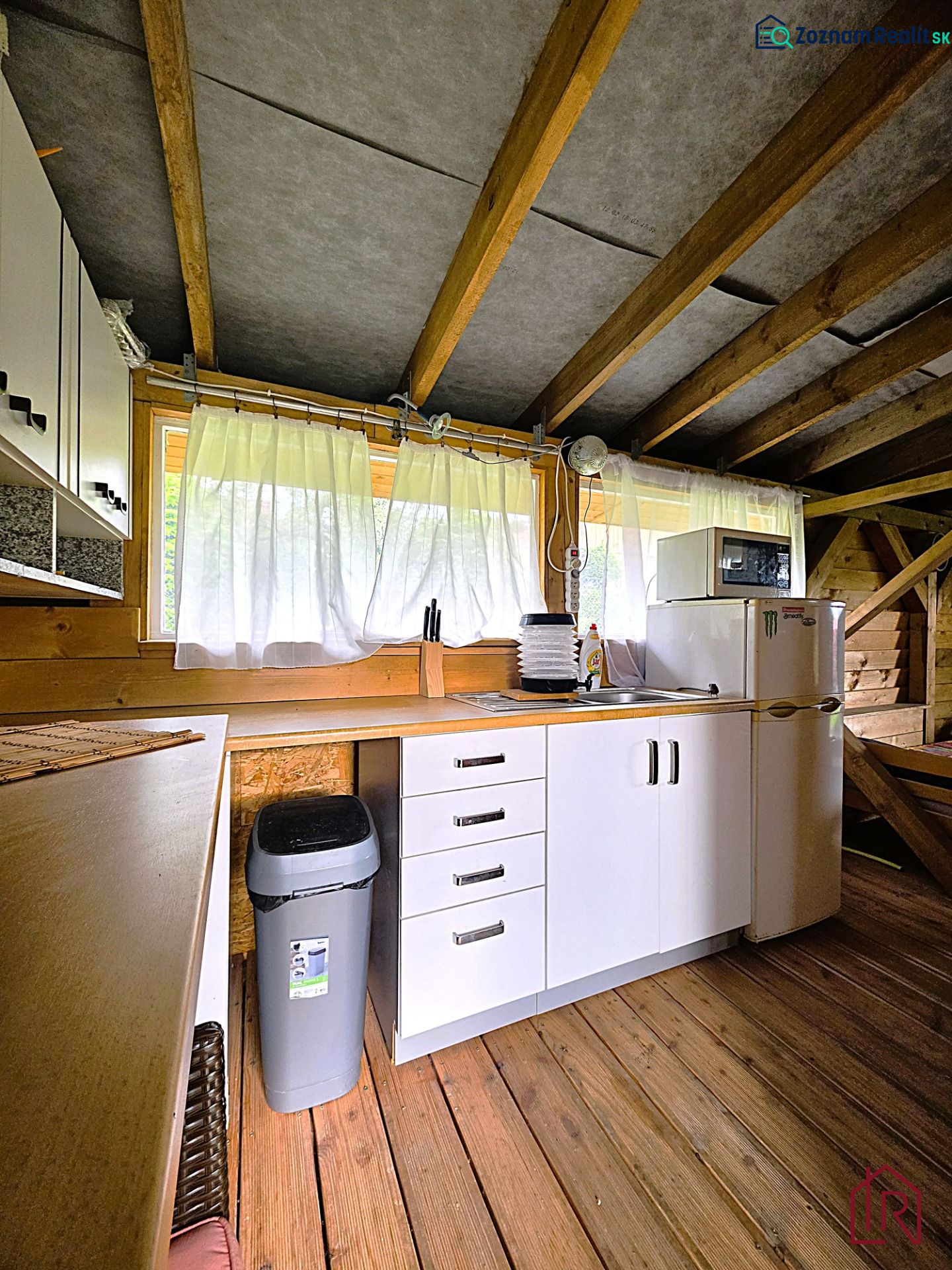 A kitchen in a cottage with white cabinets, a wood-patterned floor, and wooden beams.