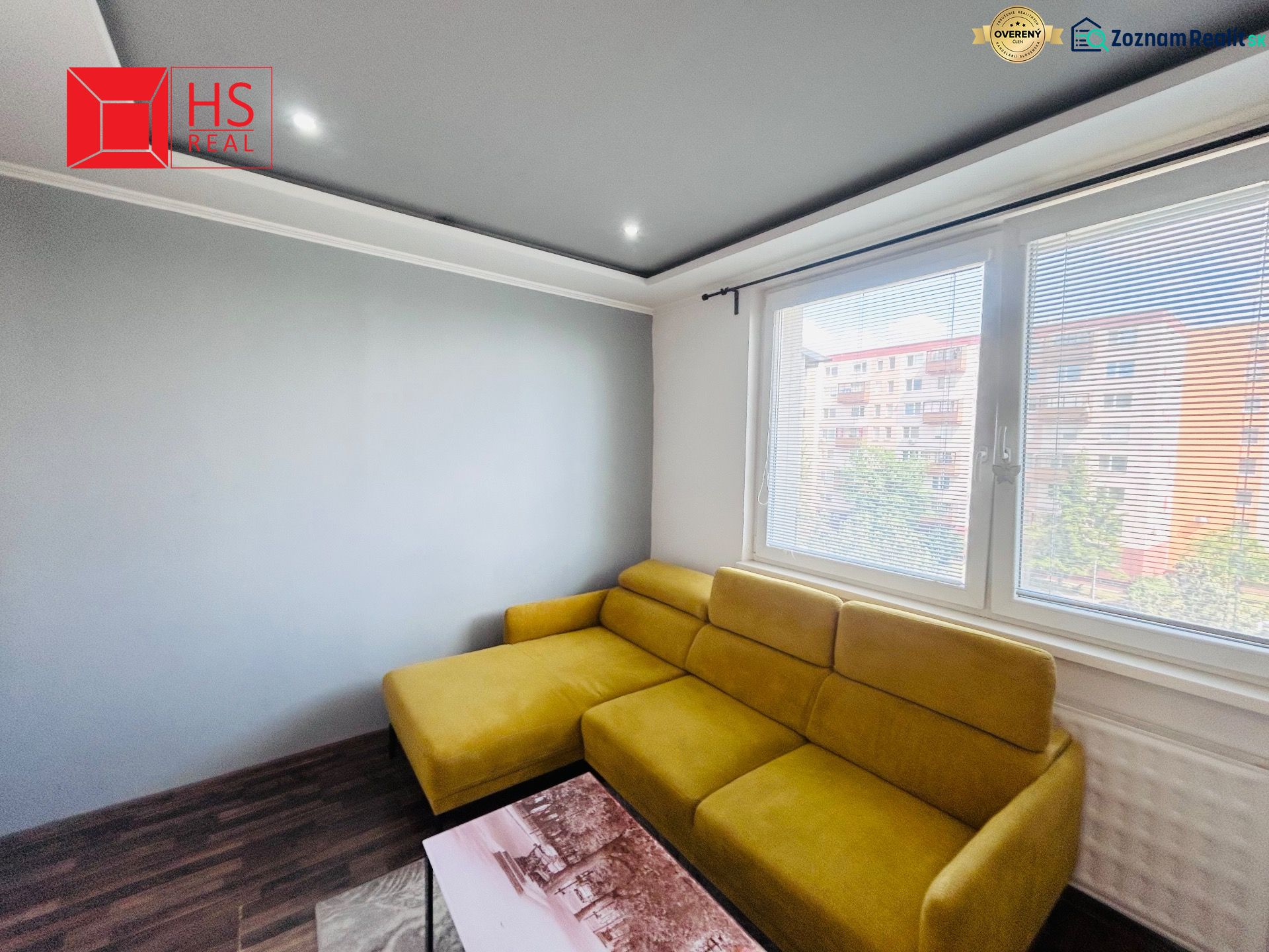 A bright living room with a comfortable yellow sofa and a wooden decor floor.