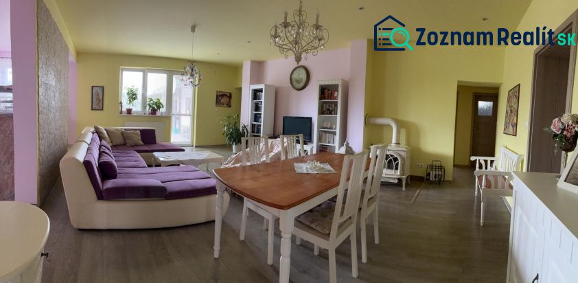 Living room in a family house, light walls, large purple sofa, dining table.