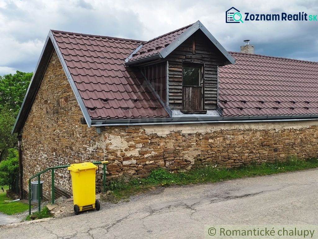 A stone cottage in Hermanovce with a metal roof and a yellow waste container.