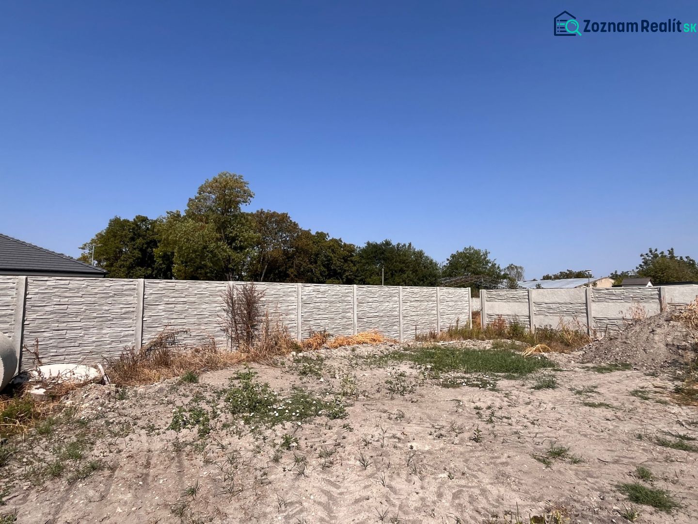 A family house in Povoda with a concrete fence, garden, and greenery under a blue sky.