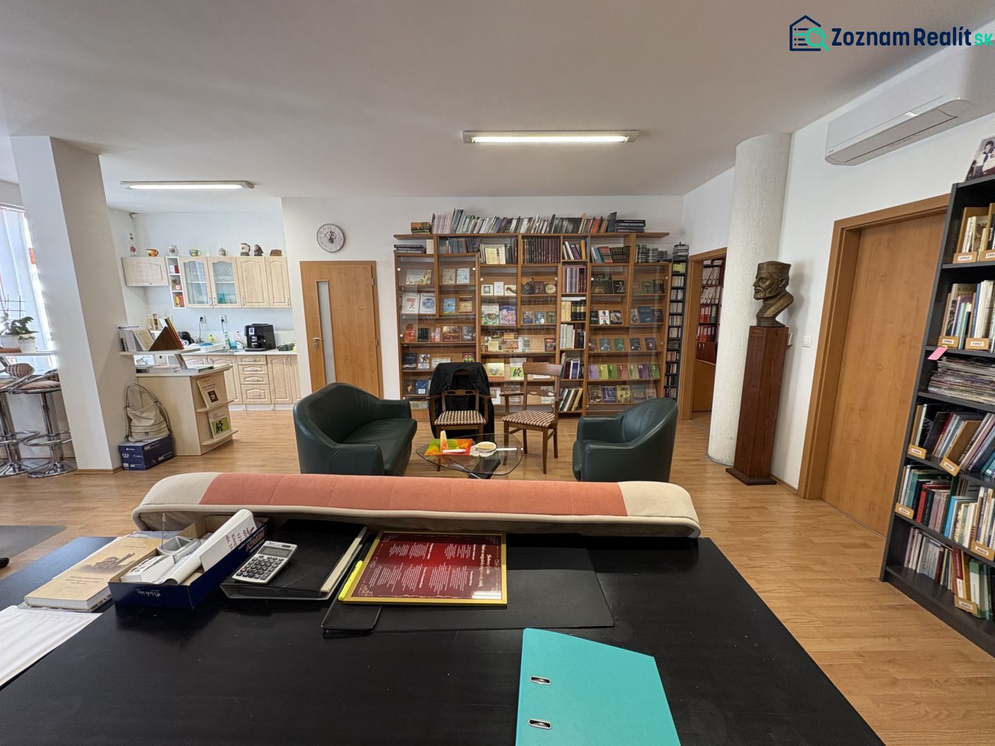 Living room with a library, kitchen, and wooden decor flooring in a 3-room apartment.
