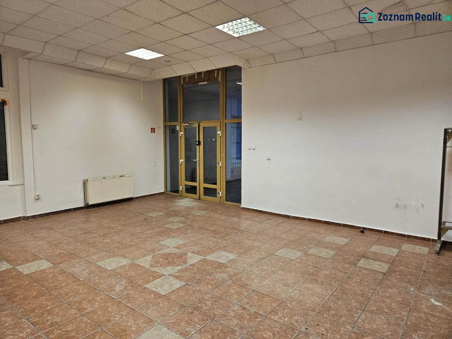 An empty commercial space with tiled flooring, white walls, and large windows.