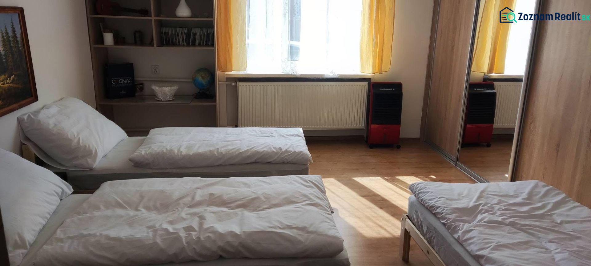A bedroom in a family house with a wooden decor floor, beds, and a built-in wardrobe.