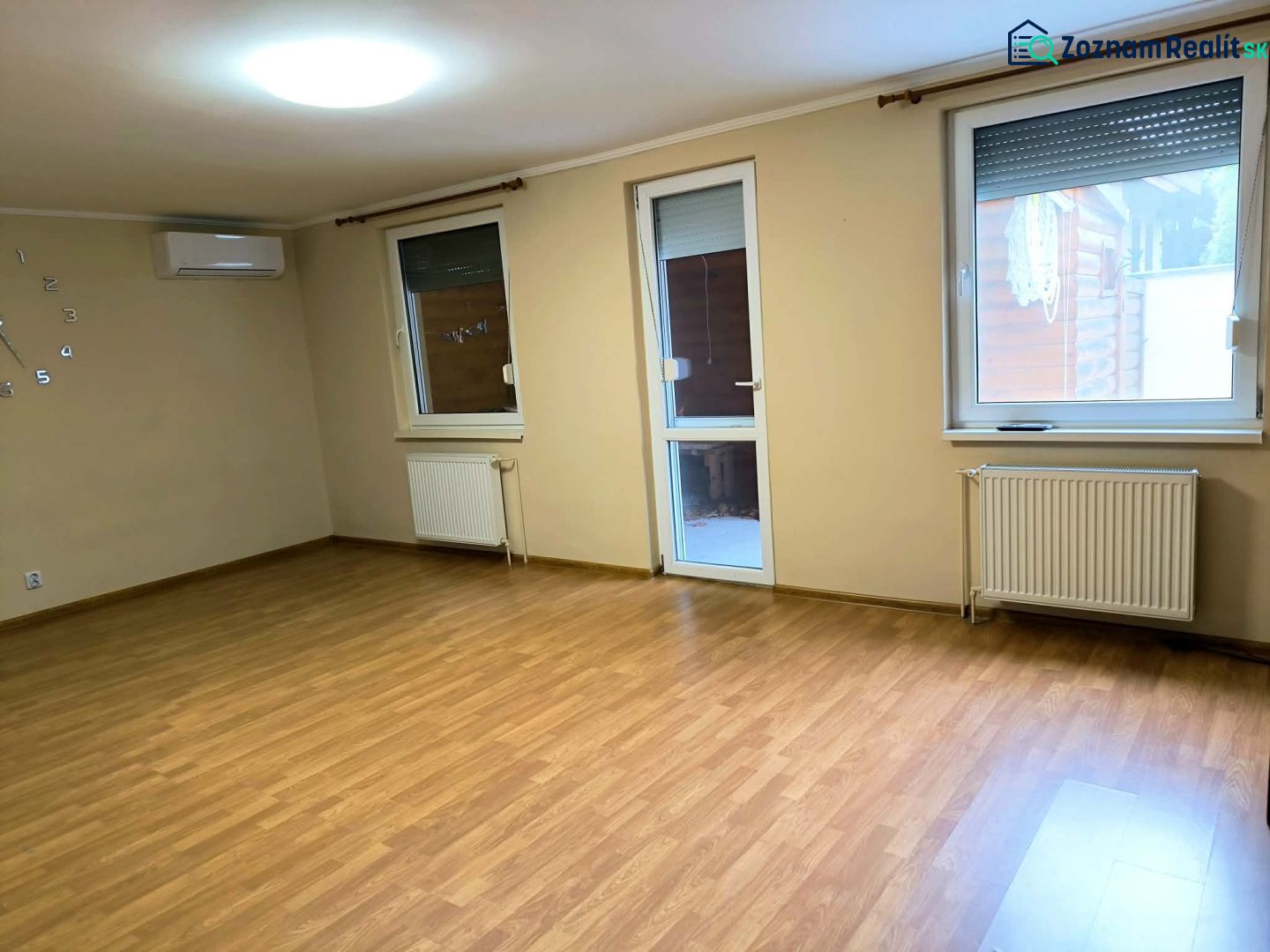 A spacious room in a family house with a wooden decor floor and windows.