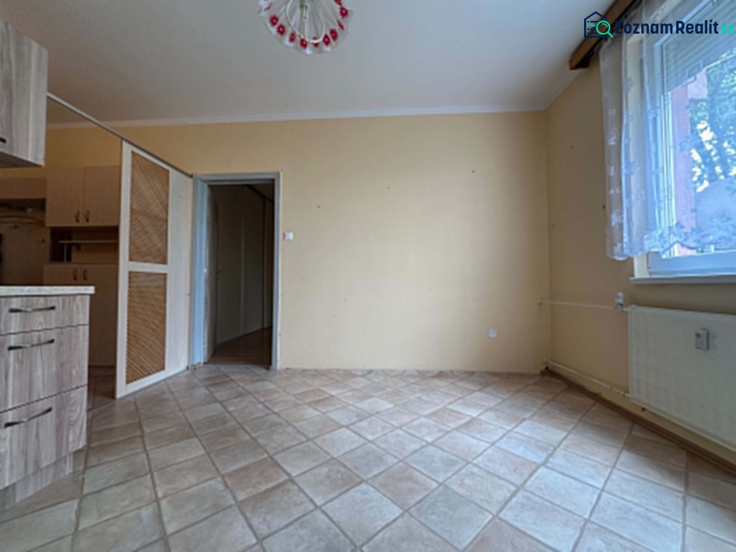 Interior of a 1-room apartment with a beige wall and tiled floor.