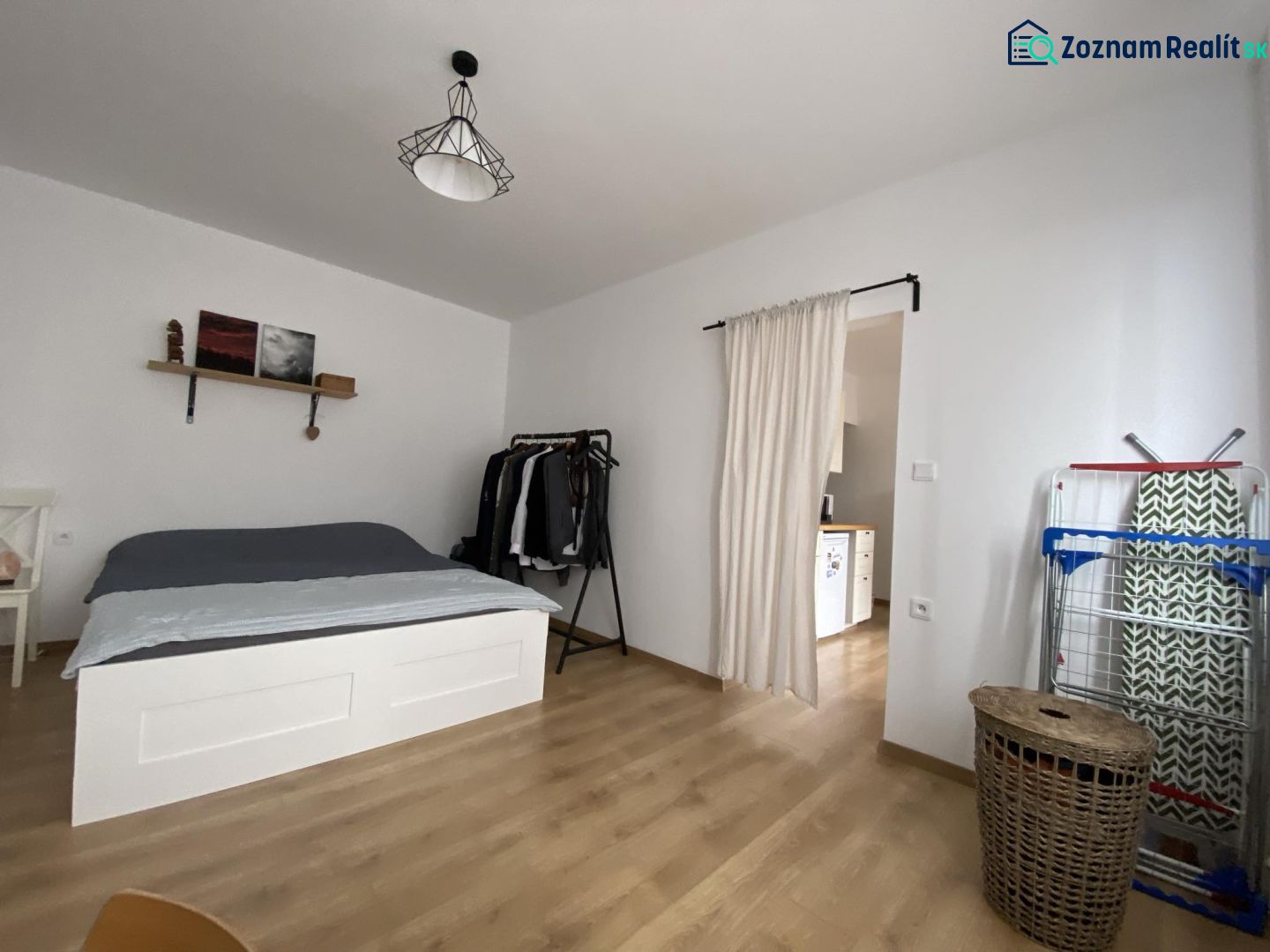 A bedroom in a studio apartment with a bed and a wooden decor floor.