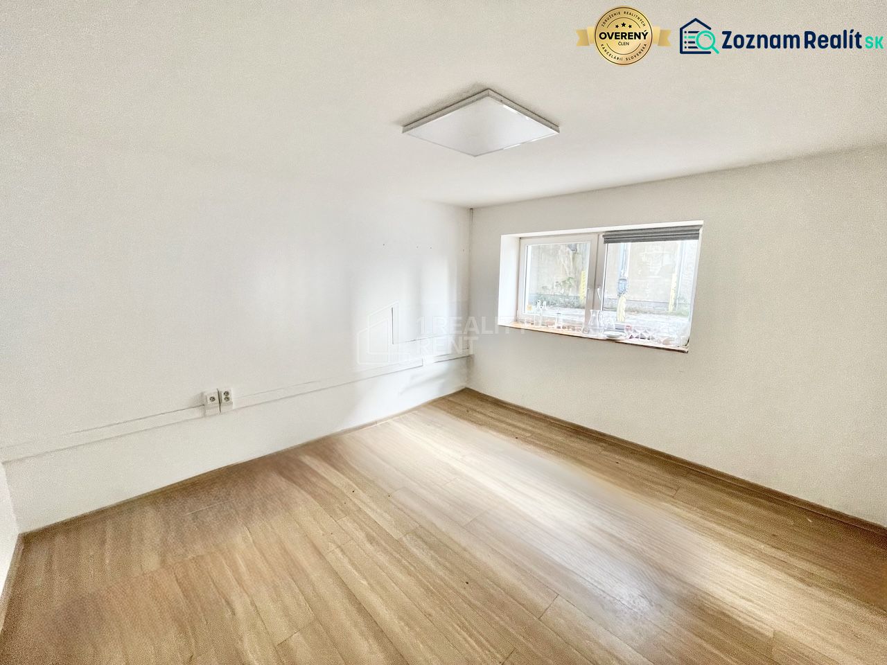 A room with a wood-patterned floor in an office, empty, with a window and white walls.