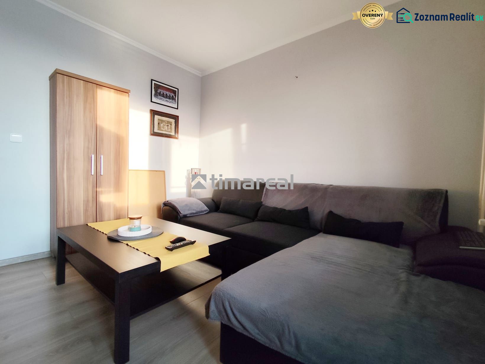 Living area of a 2-room apartment with a sofa, table, and wardrobe, floor with wooden decor.