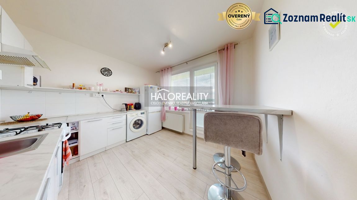 The kitchen of a two-room apartment with a wooden decor floor, white furniture, and a bar counter.
