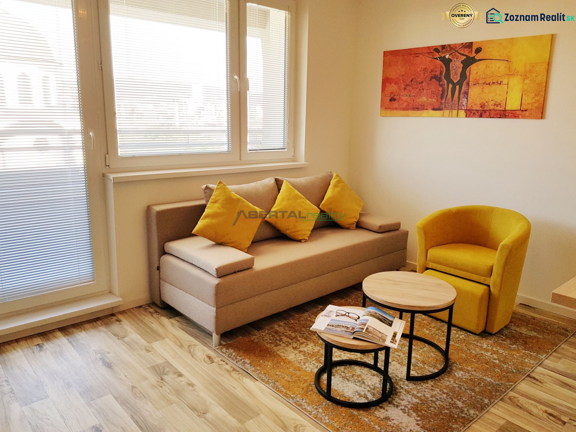 Living room in a one-room apartment with a wood-patterned floor, a sofa, and a yellow armchair.