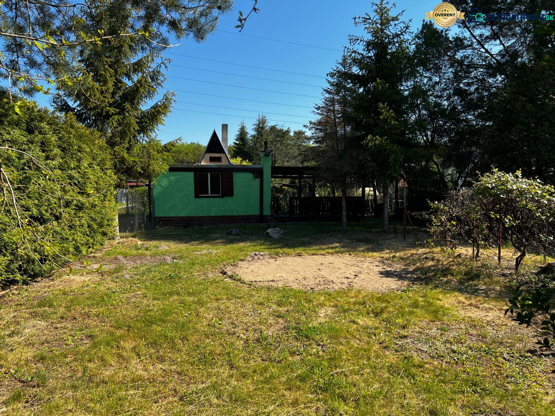 A garden in Lozorno with a cottage surrounded by greenery and trees under a blue sky.