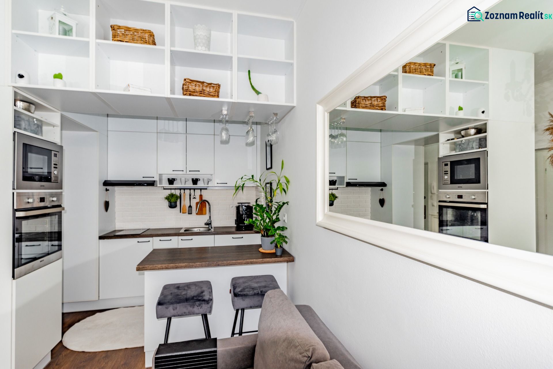 The kitchen in a 2-room apartment with white cabinets and a mirror, wood-effect flooring.